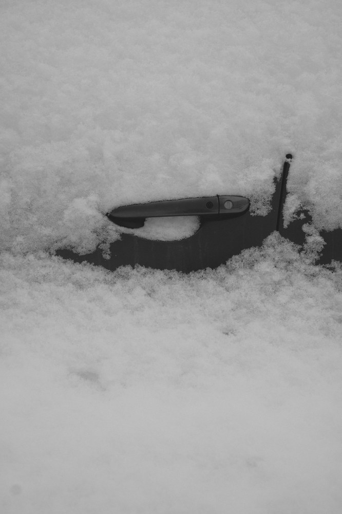 Car door handle covered in fresh snow and frost